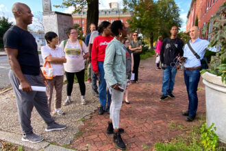 The participants of the field visit to Baltimore's Old Goucher and Broadway East neighborhoods hear Ben Zaitchik talk about the weather station installed in the backyard of Kelly Cross' house, a resident and community activist who, along with his husband Mateusz Rozanski, led the efforts to plant more trees in Old Goucher. Credit: Aman Azhar/Inside Climate News