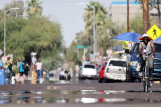 A person rides a bicycle as heat causes a visual distortion during a record heat wave in Phoenix on July 25, 2023. Credit: Mario Tama/Getty Images