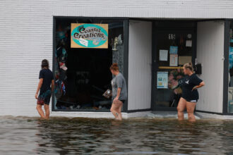 People walk through flood waters past a store with a broken window on Aug. 30, 2023 after Hurricane Idalia hit Crystal River, Fla. Credit: Joe Raedle/Getty Images